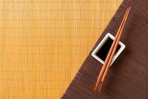 Chopsticks and bowl with soy sauce on two bamboo mat blak and yellow top view with copy space photo