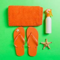 Top view of Beach flat lay accessories. sunscreen bottle with seashells, starfish, towel and flip-flop on Colored background with copy space photo