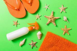 Top view of Beach flat lay accessories. sunscreen bottle with seashells, starfish, towel and flip-flop on Colored background with copy space