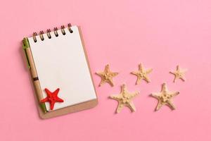 libro de notas en blanco con estrellas de mar o conchas marinas sobre un fondo rosa, concepto de vacaciones de verano foto