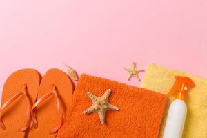 Top view of Beach flat lay accessories. sunscreen bottle with seashells, starfish, towel and flip-flop on Colored background with copy space photo