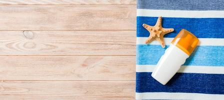 A bottle of sunscreen, striped blue towel and seashells on wooden background. Summer travel concept. Top view with copy space photo