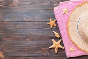 sombrero de paja, toalla rosa y estrellas de mar sobre un fondo de madera oscura. vista superior concepto de vacaciones de verano con espacio de copia foto