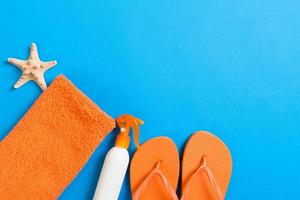 Top view of Beach flat lay accessories. sunscreen bottle with seashells, starfish, towel and flip-flop on Colored background with copy space photo
