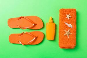 Top view of Beach flat lay accessories. sunscreen bottle with seashells, starfish, towel and flip-flop on Colored background with copy space photo