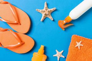 Top view of Beach flat lay accessories. sunscreen bottle with seashells, starfish, towel and flip-flop on Colored background with copy space photo
