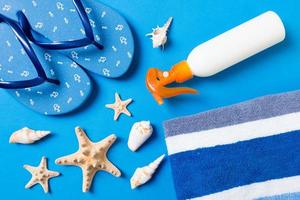 Top view of Beach flat lay accessories. sunscreen bottle with seashells, starfish, towel and flip-flop on Colored background with copy space photo