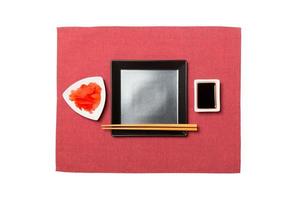 Empty black square plate with chopsticks for sushi, ginger and soy sauce on red napkin background. Top view with copy space for you design photo