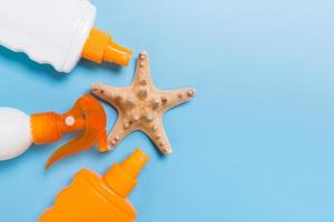 sunscreen cream with starfish and seashells in bottles on blue background, top view photo