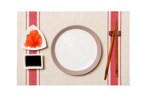 Empty round white plate with chopsticks for sushi and soy sauce, ginger on sushi mat background. Top view with copy space for you design photo