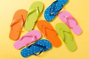 many colored flip flops on yellow background. Copy space top view photo