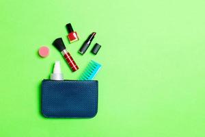 Make up products spilling out of cosmetics bag on green background with empty space for your design photo