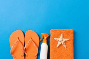 Top view of Beach flat lay accessories. sunscreen bottle with seashells, starfish, towel and flip-flop on Colored background with copy space photo