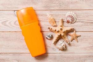 botella de crema de protección solar y conchas marinas sobre fondo de madera. concepto plano de viaje de vacaciones de verano foto