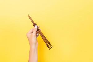 Female hand holding chopsticks on yellow background. Sushi concept with empty space for your idea photo