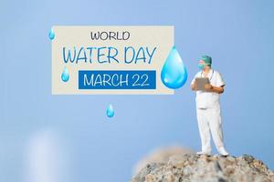 Miniature people Doctor checking text World Water Day on paper while standing atop a rock photo