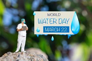 Miniature people Doctor checking text World Water Day on paper while standing atop a rock photo
