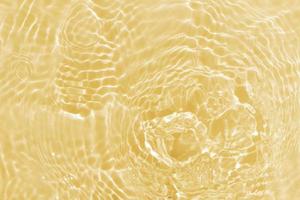 Defocus blurred transparent gold colored clear calm water surface texture with splashes and bubbles. Trendy abstract nature background. Water waves in sunlight with caustics. Yellow water shinning photo