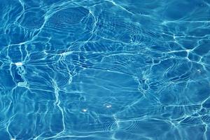 desenfoque borroso transparente color azul claro agua tranquila textura superficial con salpicaduras y burbujas. fondo de naturaleza abstracta de moda. ondas de agua a la luz del sol con cáusticos. agua azul brillando foto