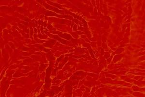 Defocus blurred transparent red colored clear calm water surface texture with splashes and bubbles. Trendy abstract nature background. Water waves in sunlight with caustics. Red water shinning photo
