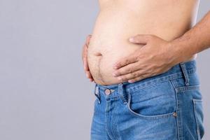 hombre gordo parado y mostrando su estudio de barriga en fondo gris con espacio de copia para texto o diseño. gente gorda y concepto saludable foto