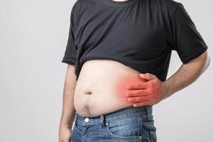 Body pain, hip pain or effect from liver problem Fat man using his hand and pressing on hip position. Studio shot on grey photo