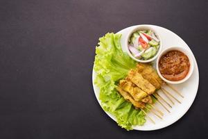 satay de cerdo con salsa de maní y pepinillos que son rodajas de pepino y cebollas en vinagre. aislado sobre fondo blanco foto