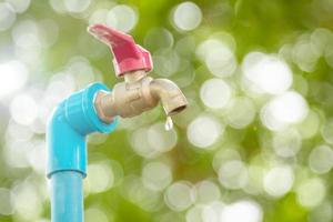 Macro water faucet with one water dripping in garden with green nature bokeh and blur photo