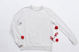 Close up white blank template sweatshirt with copy space and Christmas Holiday concept. Top view mockup hoodie and red holidays decorations on white background. Happy New Year accessories. Xmas outfit photo