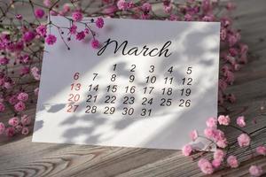 March 2022 calendar and pink flowers in the spring sunshine photo