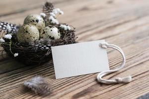 nido con huevos de codorniz y tarjeta blanca en blanco para texto. etiqueta de maqueta. tarjeta de pascua decoración de pascua en estilo rústico. decoración de pascua ecológica natural foto