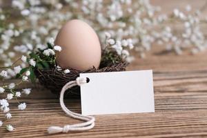 nido con un huevo y una tarjeta blanca en blanco para texto. etiqueta de maqueta. tarjeta de pascua decoración de pascua ecológica natural. foto