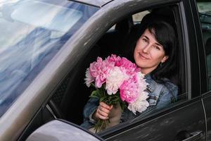 mujer sonriente joven con un ramo de flores sentado en el coche foto