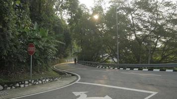 calle local en la colina con gente montando en bicicleta hasta la colina bajo los árboles del bosque tropical