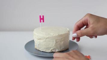 coccion y decoracion de torta velas en forma de letras. niña mano pastelero en la cocina decorando pastel de crema blanca palabra - feliz. mujer joven en la cocina hace un hermoso pastel de cumpleaños. video