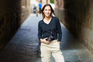 mujer sonriente con cámara fotográfica mirando a la cámara en una calle angosta foto