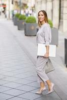 confiada mujer de negocios bien vestida con netbook paseando por la ciudad foto