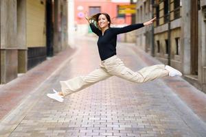 Excited young woman jumping on paved street and smiling photo