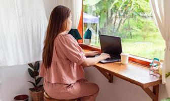 una mujer feliz con una camisa rosa se sienta en una computadora portátil que funciona. mujer de negocios ocupada trabajando en una laptop en un café foto