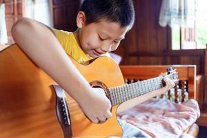 A white Asian boy with a dimple on his cheek happily practiced playing the acoustic guitar. photo