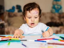 Happy little boy draws with colorful markers on a piece of paper photo