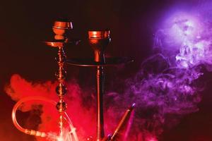 Modern hookah, shisha on a smoky black background with colored lighting and smoke. Close up photo