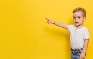 A little boy on a yellow background points to the background. Copy space. photo