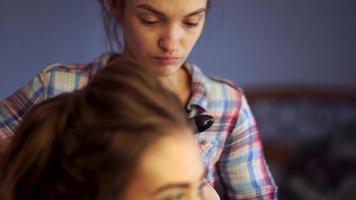 blonde stylist girl makes hairstyle to a young woman in hair studio video