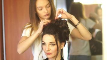 Young blonde stylist girl makes hairstyle to a woman in hair studio video