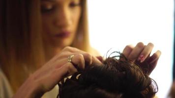 blonde stylist girl makes hairstyle to a young woman in hair studio video