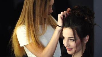 Young blonde stylist girl makes hairstyle to a woman in hair studio video