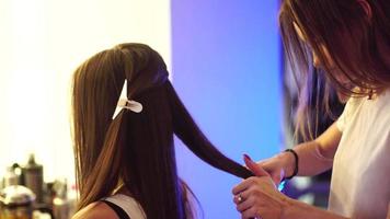 Young blonde stylist girl makes hairstyle to a woman in hair studio video