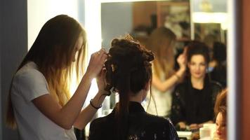 Young blonde stylist girl makes hairstyle to a woman in hair studio video