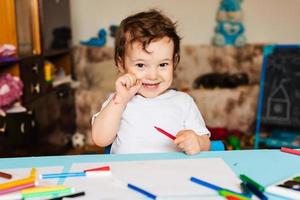 Happy little boy draws with colorful markers on a piece of paper photo